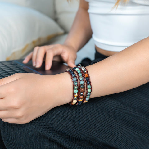 A woman wearing a triple-layer matte African Turquoise and Picasso Jasper wrap bracelet with dark leather.