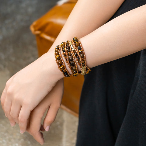 A woman wearing a five-layer Tiger’s Eye wrap bracelet with gold beads and a brown leather cord.