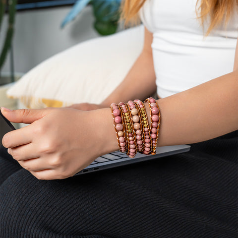 Person wearing stacked Rhodochrosite bracelets on wrist while resting hand on laptop