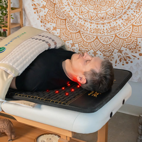 A man lies on a HealthyLine Jet 7224 InfraMat Pro with red photon lights and a 360-wrap for professional wellness therapy.