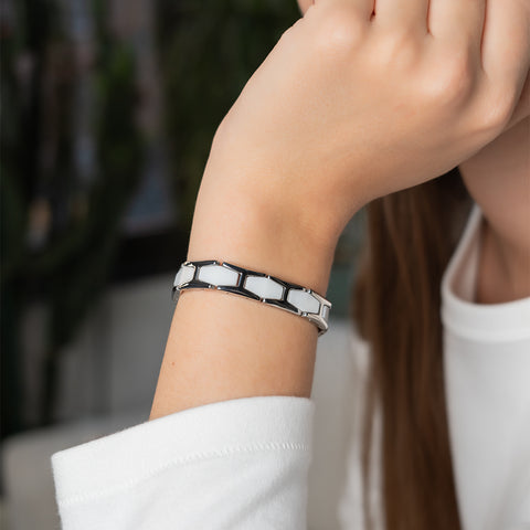 A woman wearing a white ceramic and silver stainless steel magnetic link bracelet on her wrist.
