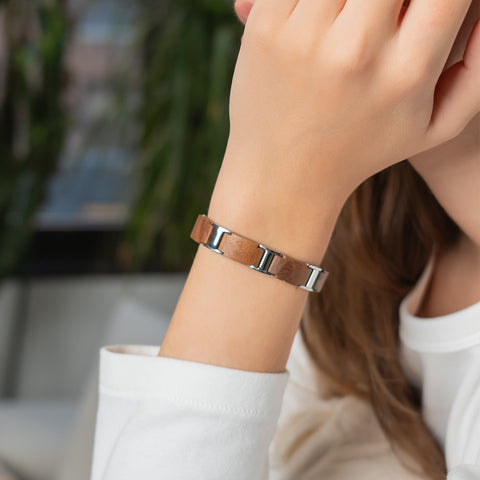 A woman wearing a brown wood and silver stainless steel magnetic link bracelet on her wrist.