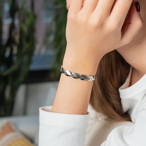 A woman wearing a silver stainless steel energy bracelet with teardrop-shaped links on her wrist.