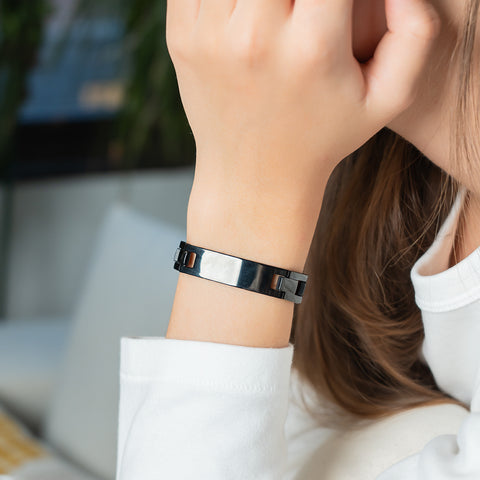 A woman wearing a wide silver stainless steel energy bracelet with a double-row link design on her wrist.