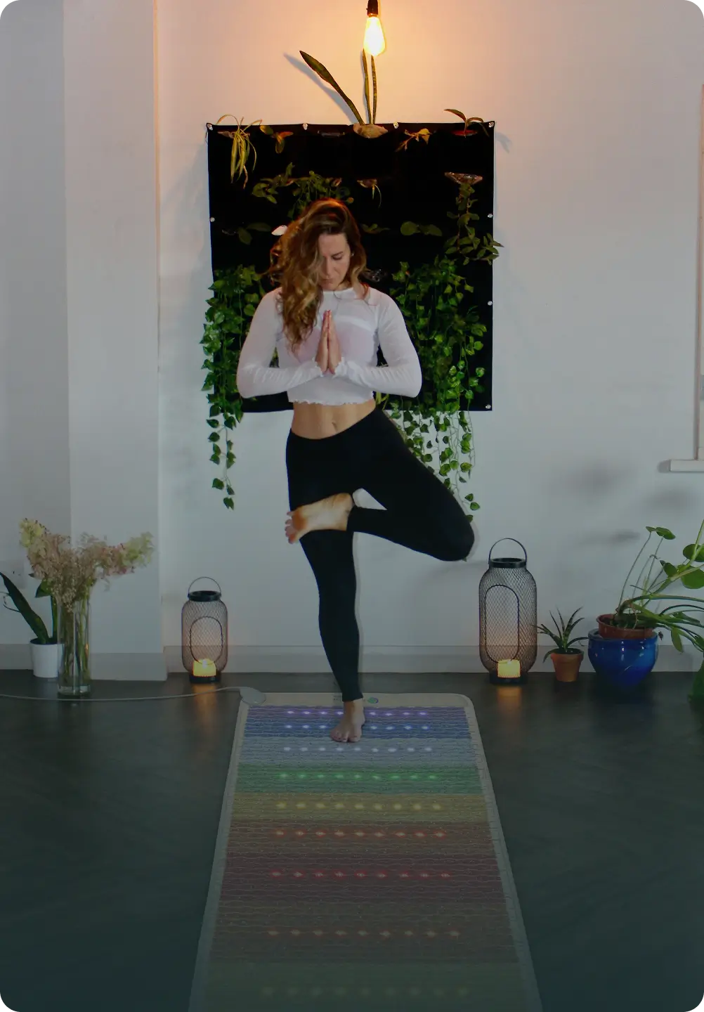 Woman in a tree pose on the HealthyLine Rainbow Chakra Mat 7428, showing multicolored LED bands in a yoga studio