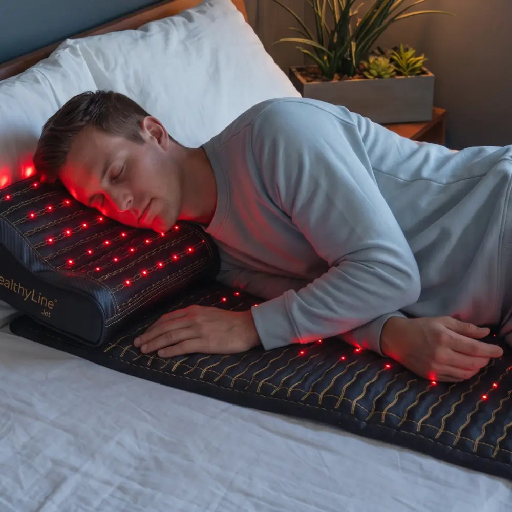 Man asleep with head on HealthyLine Jet Pillow and arm on Jet 7428 mat, red LED light therapy active.
