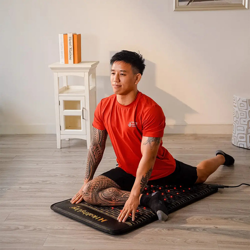 Man stretching on the HealthyLine Jet Mat 4020 with glowing red infrared LEDs on a hardwood floor