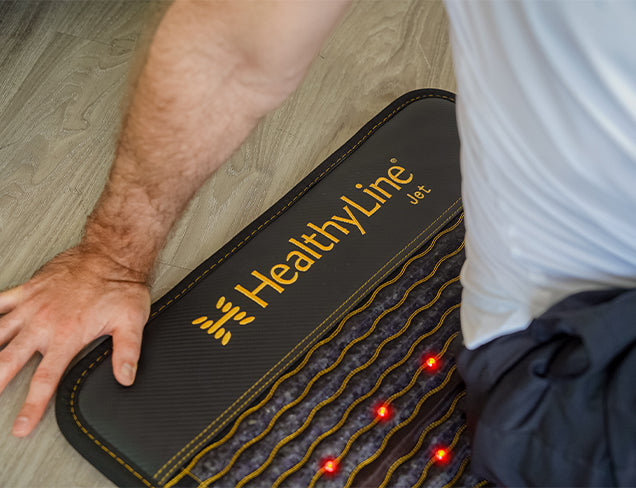 Close-up of a person lying on a HealthyLine JET 40x24 mat with active red infrared LEDs visible on the wavy surface