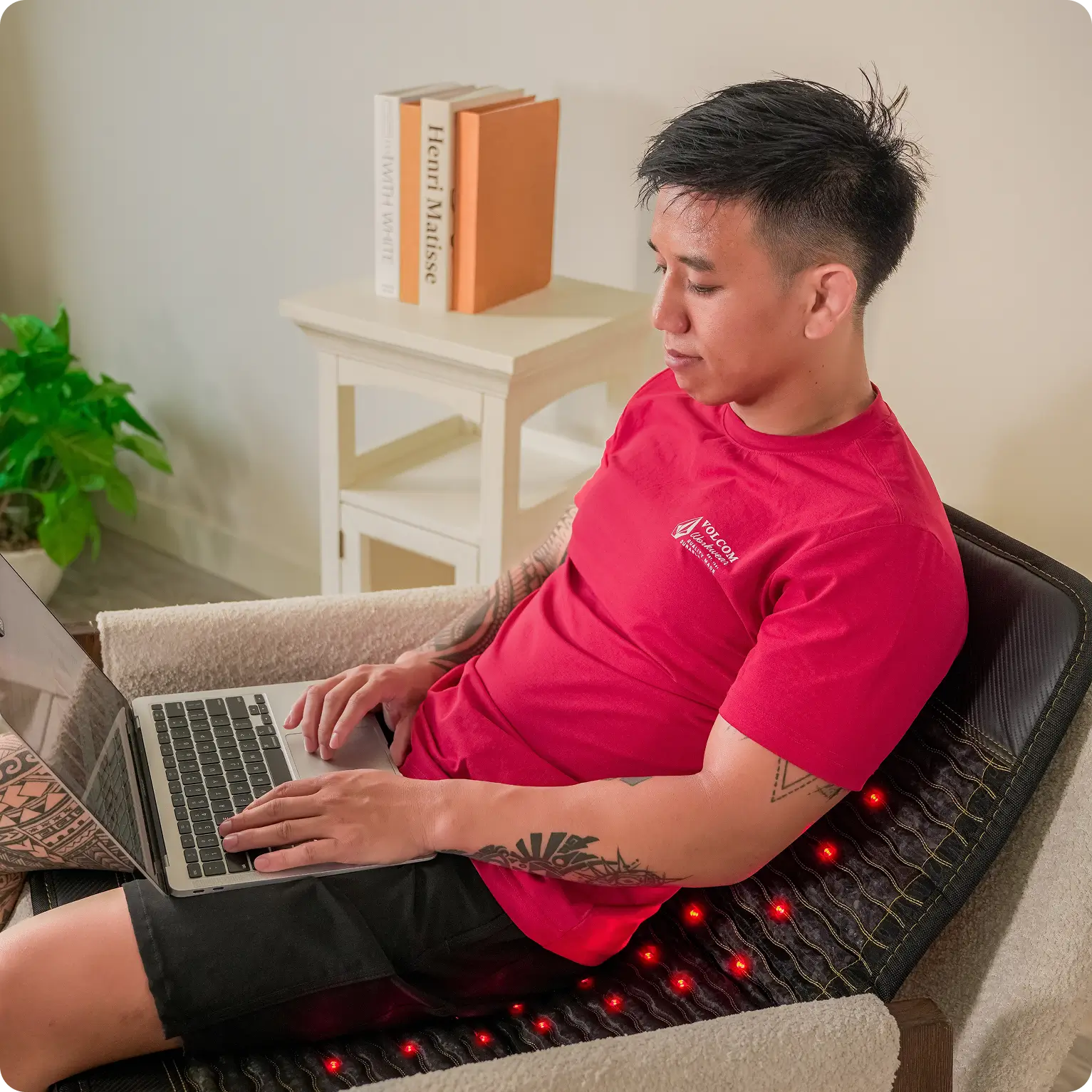 Man using a laptop while seated on the HealthyLine Jet Mat 4024 with glowing red infrared LEDs in a living room