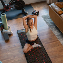 Woman stretching with arms raised on the Jet mat on a home gym floor, red photon lights glowing beneath her