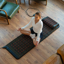 Woman sitting cross-legged in meditation pose on the Jet 72x24 mat with red photon lights glowing on a wood floor