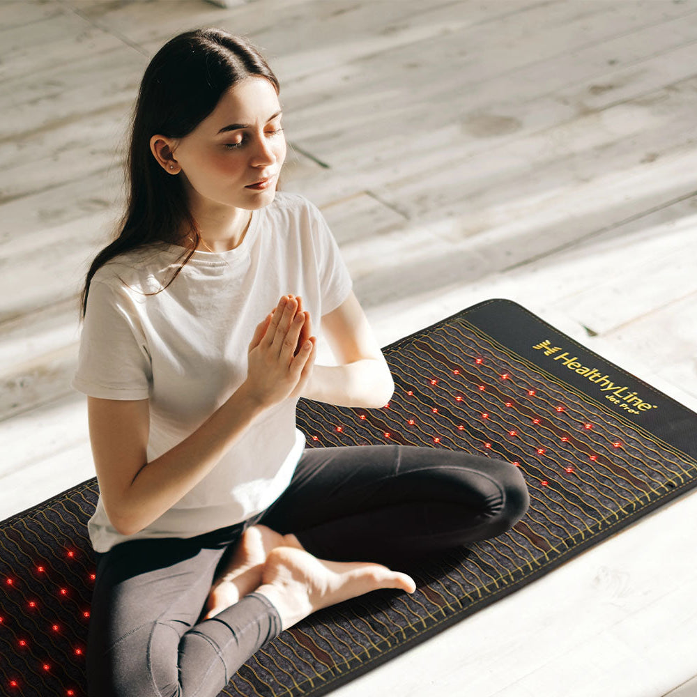 Woman meditating in a cross-legged pose on a HealthyLine Jet Pro+ 74x28 infrared therapy mat with red lights