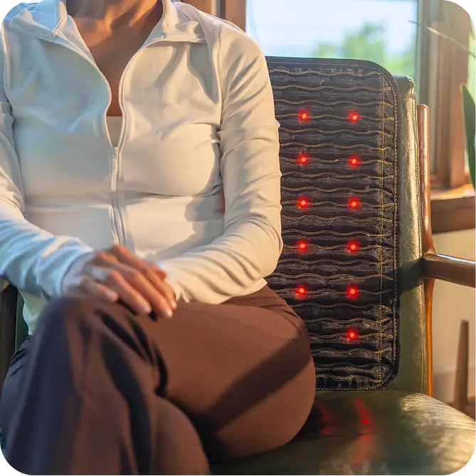 Person seated in a chair with the Jet mat 20x20 as a back pad, red light therapy LEDs illuminated