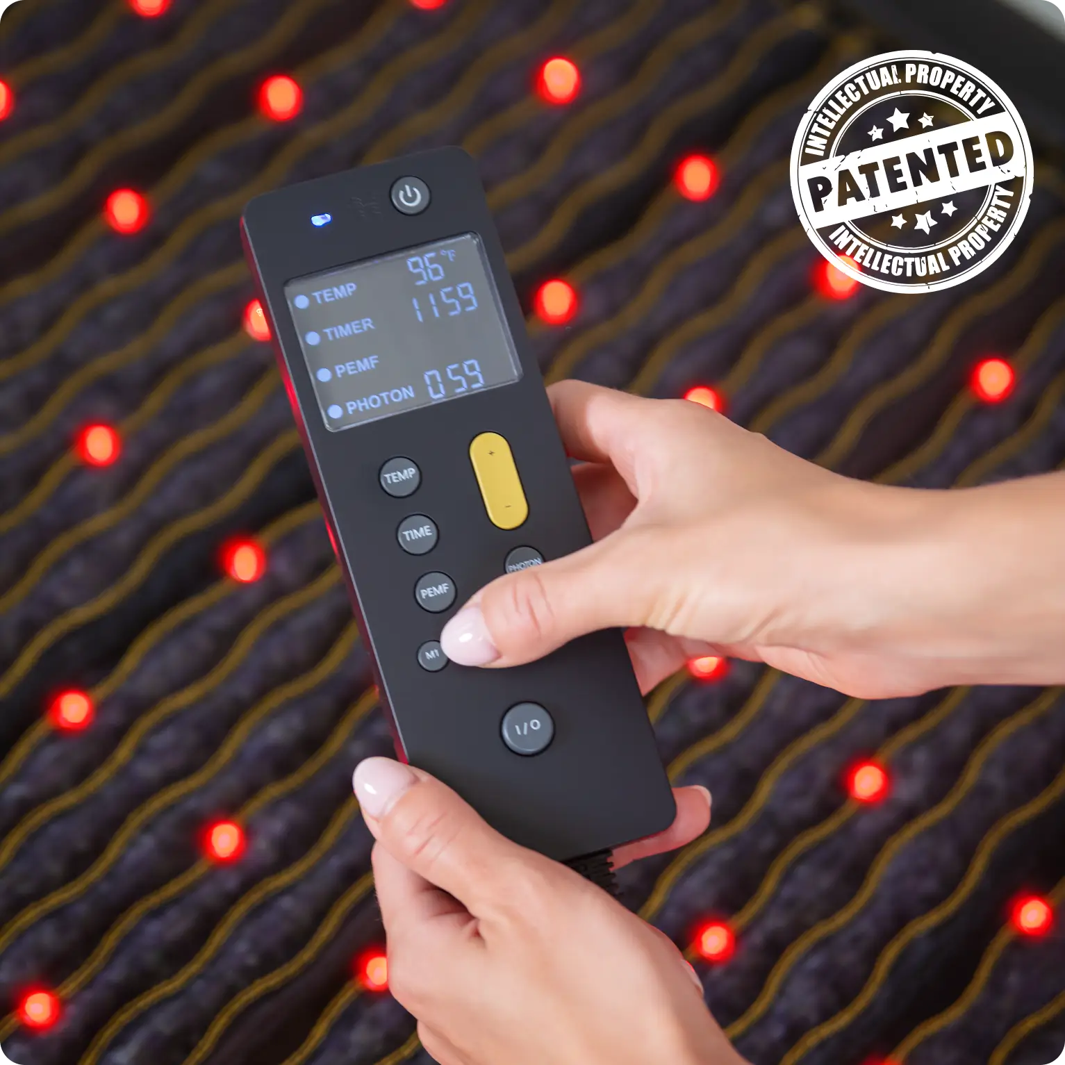 Hands holding the patented HealthyLine Jet Controller displaying temp, timer, PEMF, and photon settings over a glowing mat