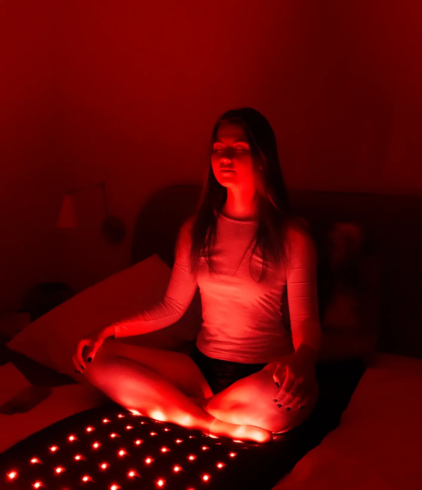Woman meditating cross-legged with her feet resting on a Jet mat in a dim, red-lit room.