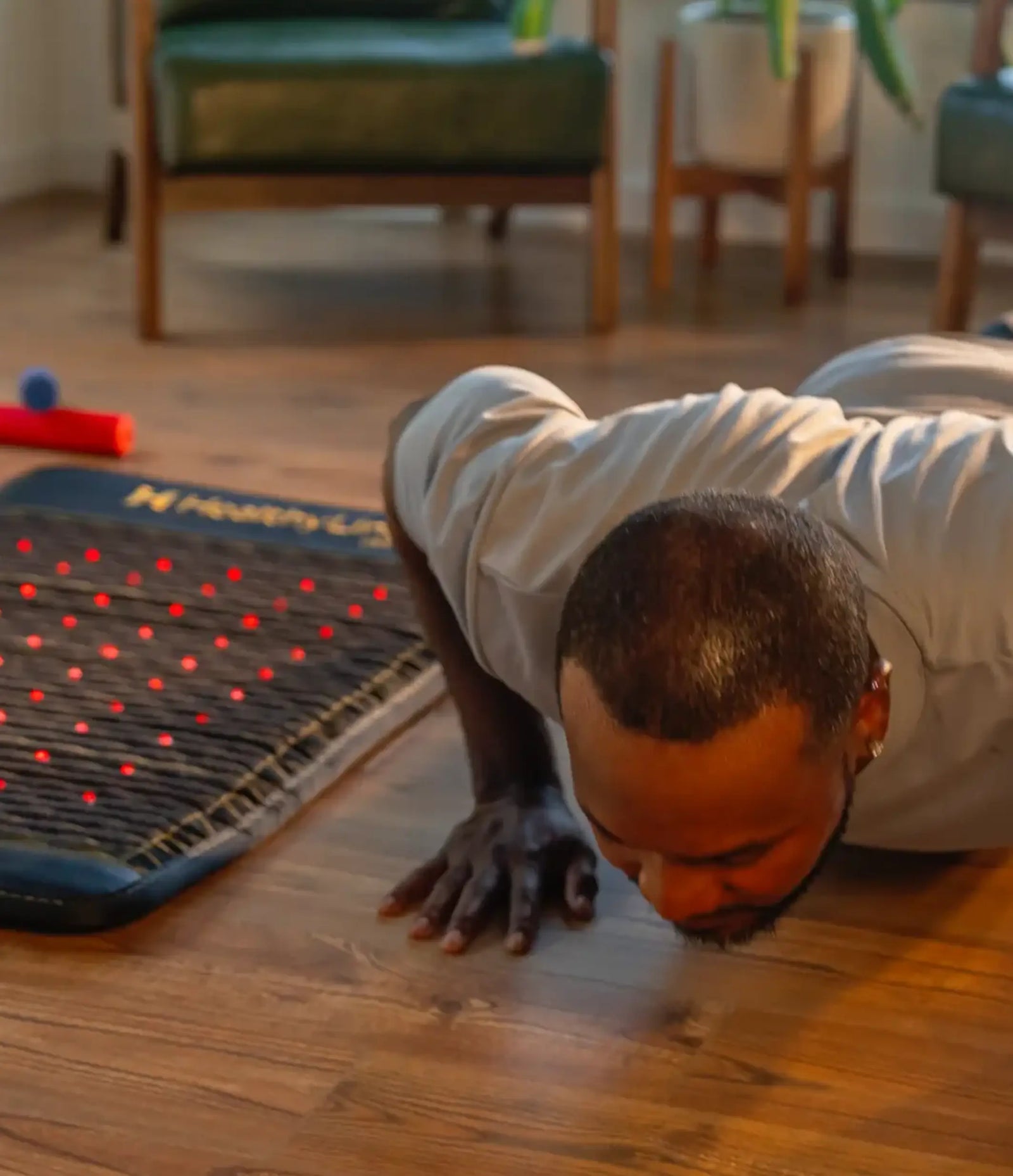 Man doing a push-up on a hardwood floor beside a Jet mat with glowing red LED therapy lights.