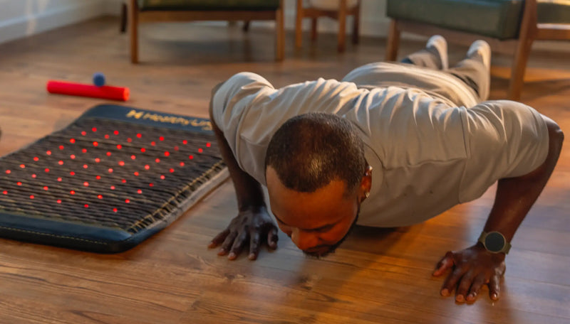 Man doing a push-up on a hardwood floor beside a Jet mat with glowing red LED therapy lights.