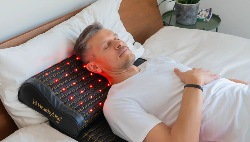 Man sleeping on his back with a HealthyLine Jet mat and pillow supporting his neck, red LEDs glowing.