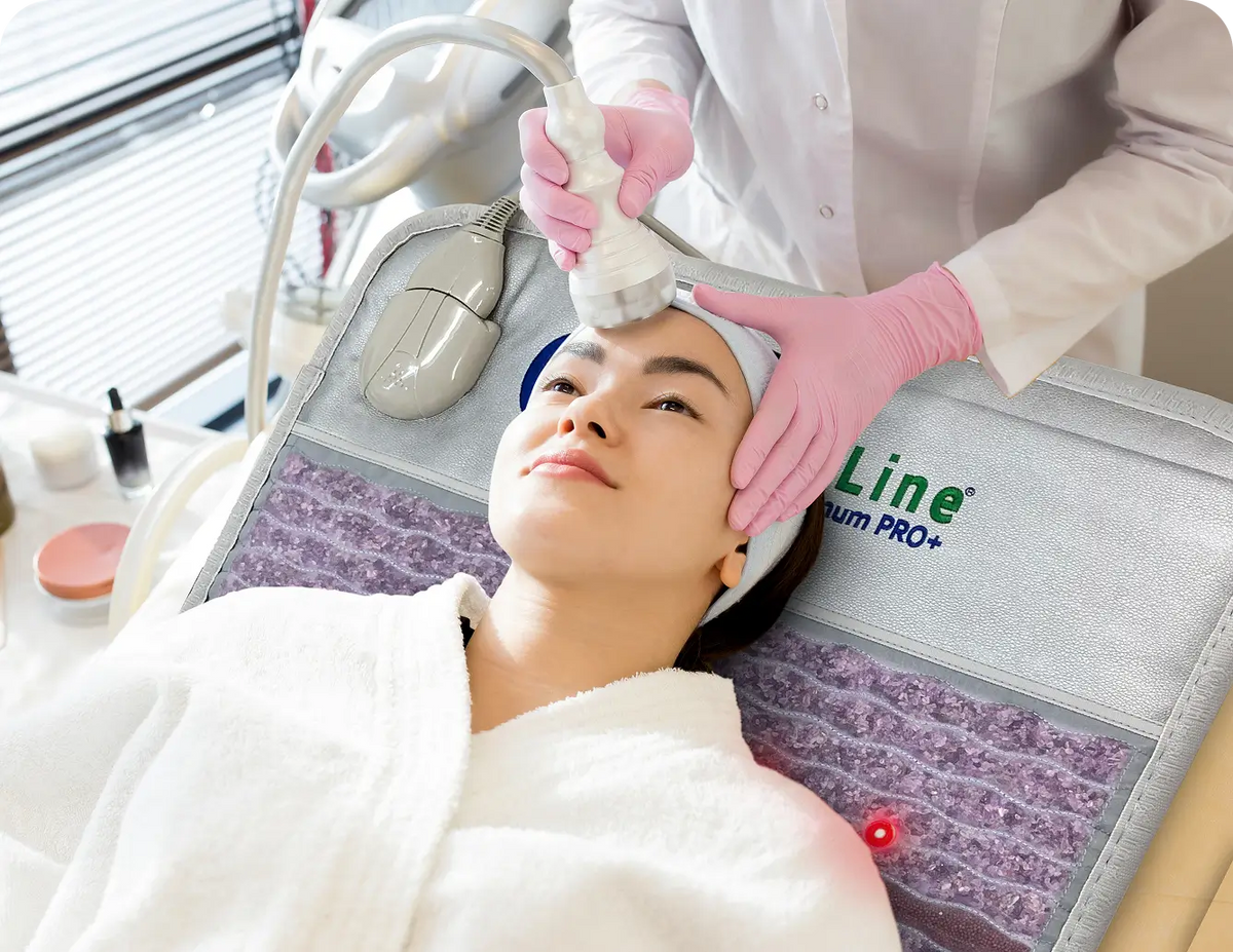 Woman receiving a facial device treatment while lying on the HealthyLine Platinum PRO+ Mat 7428 in a clinical spa