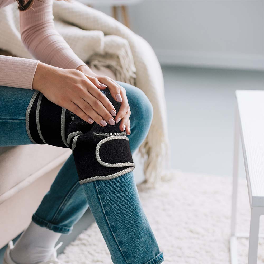Person wearing Portable Heated Belt Knee around knee, flexible wrap design with amethyst and tourmaline gemstones in use
