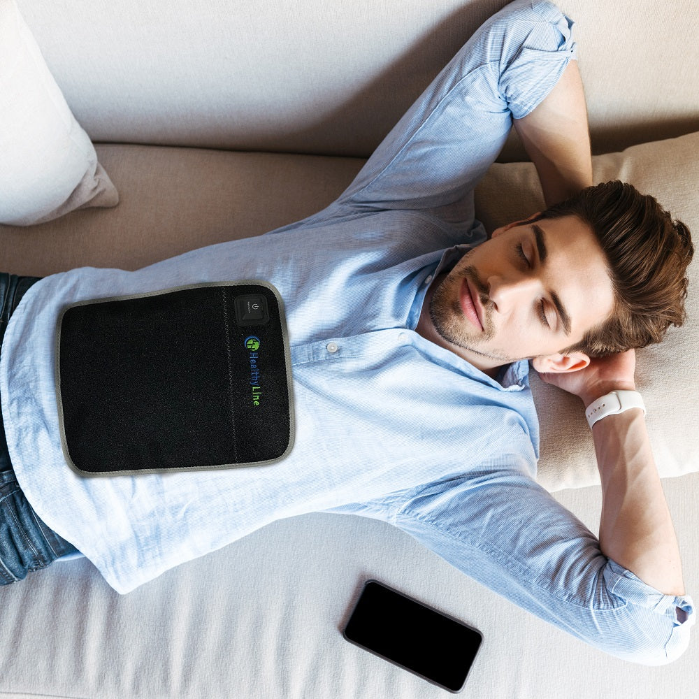 Person using Portable Heated Flat Pad on their abdomen, cordless flexible design with gemstone therapy at home
