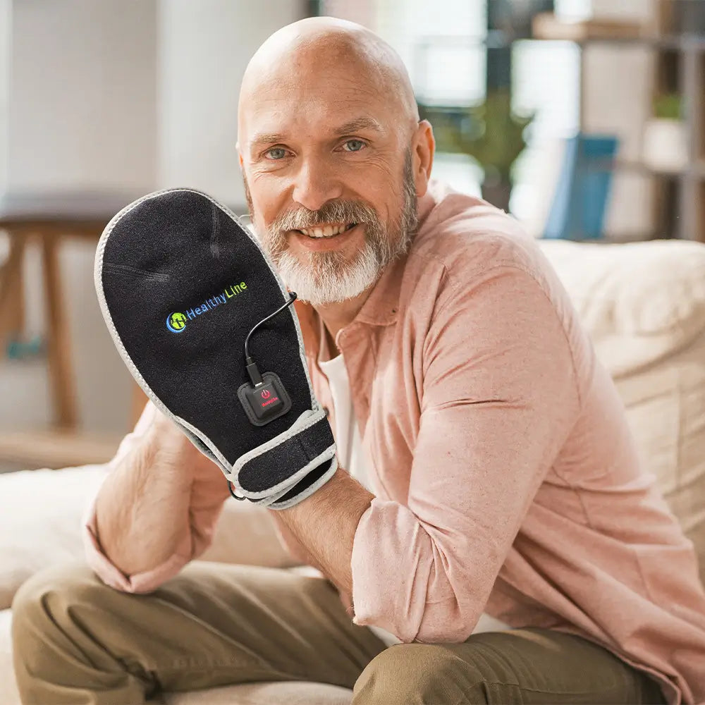 Smiling man holding up a HealthyLine portable heat therapy hand mitt on his couch.
