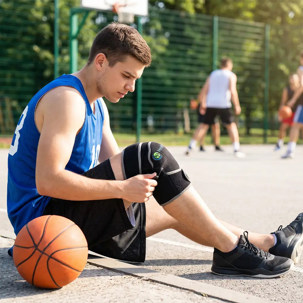Basketball player sitting on court adjusting a HealthyLine portable knee heat pad
