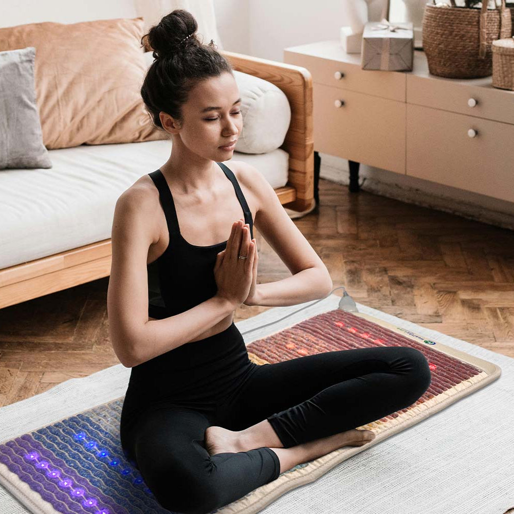 Woman meditating in prayer pose on a HealthyLine Rainbow Chakra 50x24 mat with multicolor photon lights