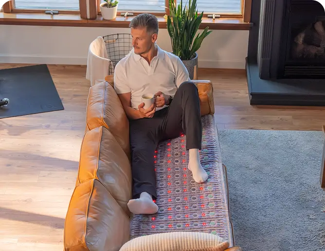 Man holding a mug while relaxing on a sofa with the HealthyLine TAJ Mat 7224 and active red infrared LEDs