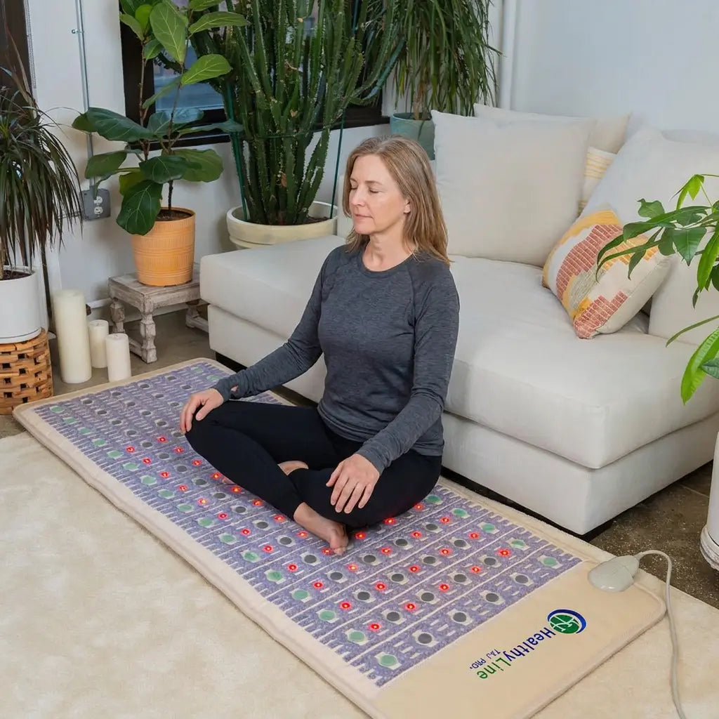 Woman meditates cross-legged on a HealthyLine TAJ Mat 7428 with glowing red photon lights, laid on a living room rug
