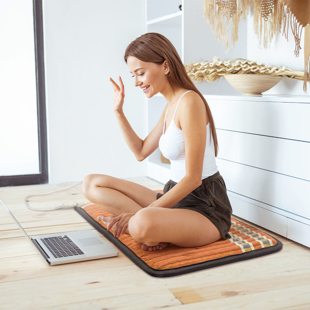 Woman sitting cross-legged on a HealthyLine TAO 3220 infrared gemstone mat, smiling during a video call
