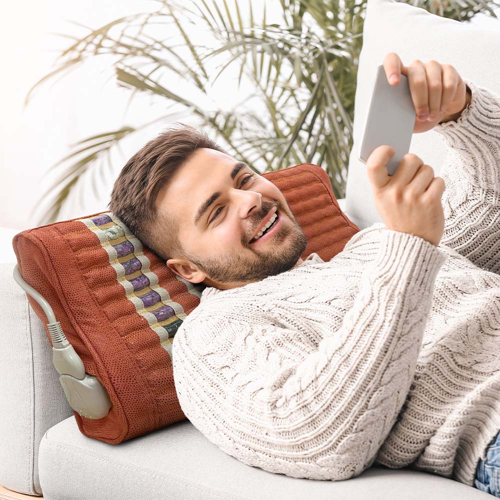 Man reclining on a sofa using a tablet, with his head resting on a HealthyLine TAO gemstone therapy pillow