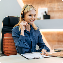 Woman smiling and working at a desk with a headset, seated in a HealthyLine TAO 40x18 chair mat
