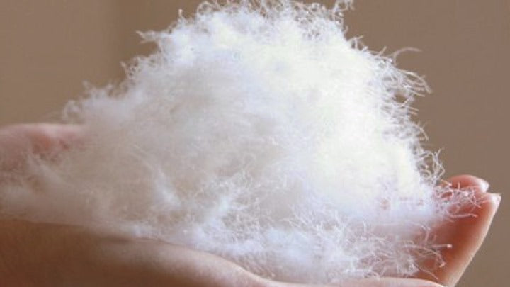 A person holding a fluffy mound of white raw silk filling to show its lightweight and down-like texture
