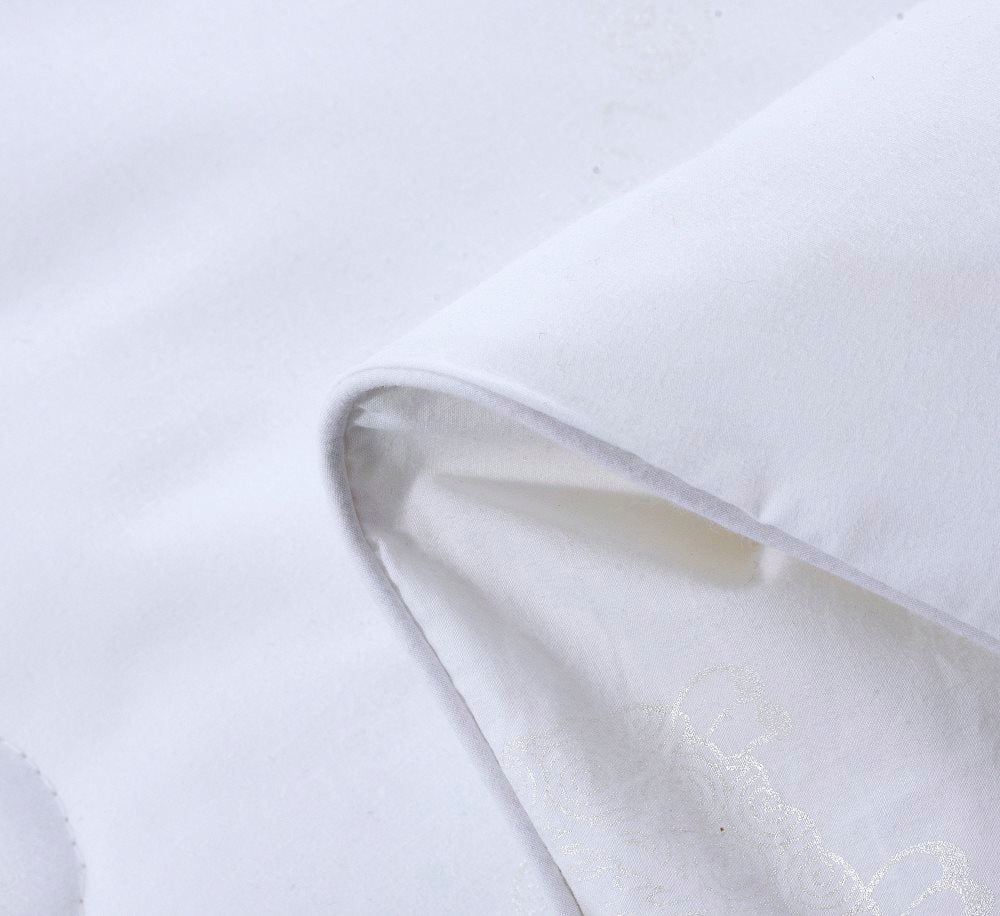 Close-up of a white HealthyLine quilt corner, showing the piped edge finish and subtle embossed fabric pattern.
