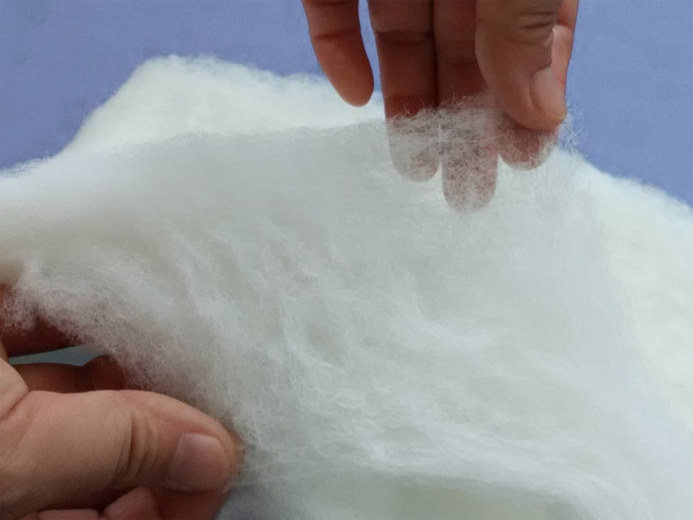 Hands pulling apart a thick layer of white natural silk batting to demonstrate the comforter's soft, airy loft.

