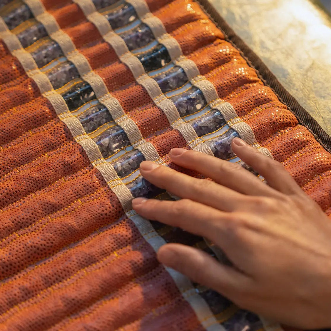 
                  
                    Extreme close-up of a TAO Mat's mesh surface, showing rows of crushed amethyst, tourmaline, and obsidian gemstones.
                  
                