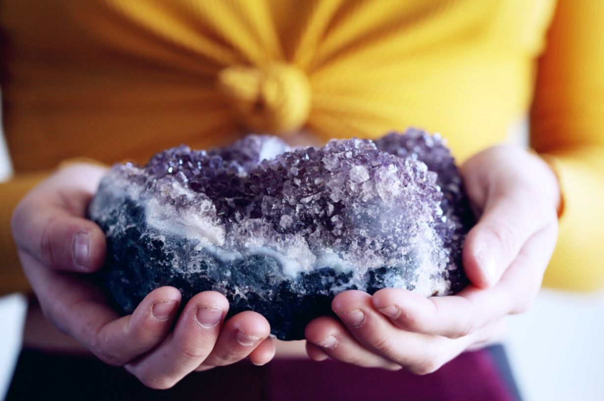 Person holding a large natural amethyst gemstone in their hands